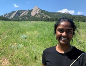 Sindhu Shankar, smiling in front of a meadow and mountain scenery in the background