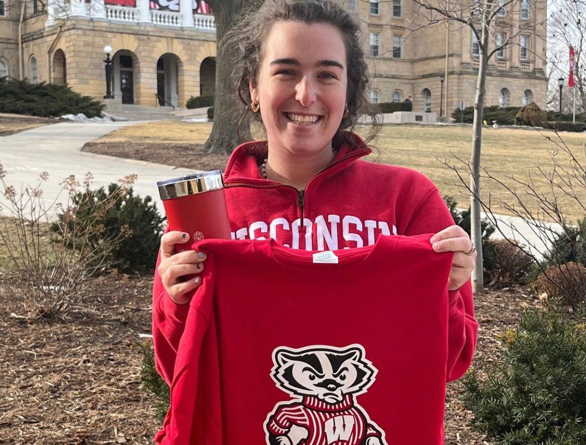 Sara Kaska holding a red Badger t-shirt and cup and smiling