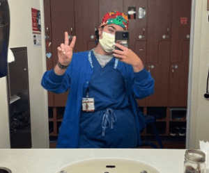 Sara Kaska in scrubs, taking a selfie in a mirror, masked