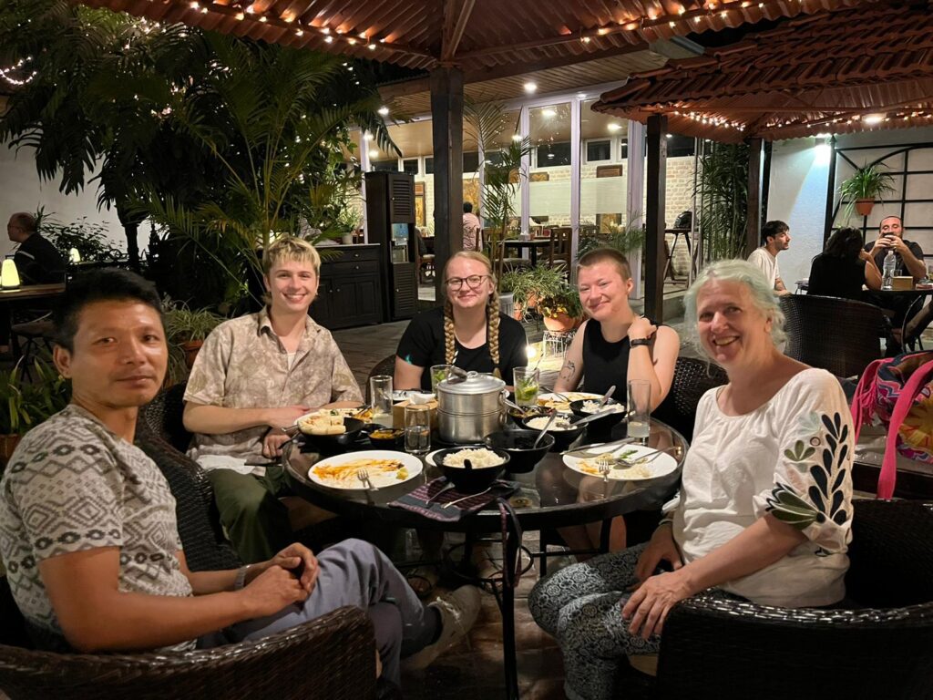 Un grupo de estudiantes, profesores y amigos en la mesa exterior del restaurante, sonriendo