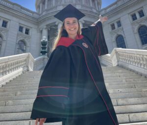 Caroline Muehlenkamp posing in her cap and gown in front of the State Capitol building