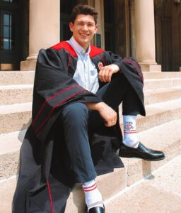 Samuel Peterson in his graduation gown, smiling, sitting on steps