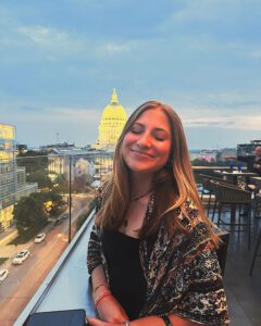 Summer student with medium length brown hair smiling on rooftop with Wisconsin capital building in the backdrop