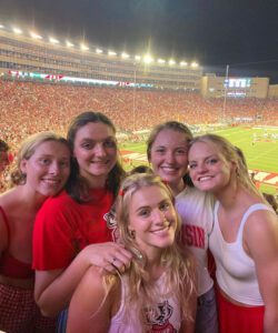 5 students in Wisconsin Badger spirit-wear smile with Camp Randall stadium in backdrop.
