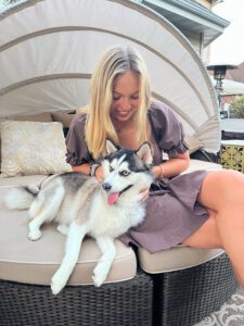 Summer Student seated on outdoor patio bed with medium-sized husky dog