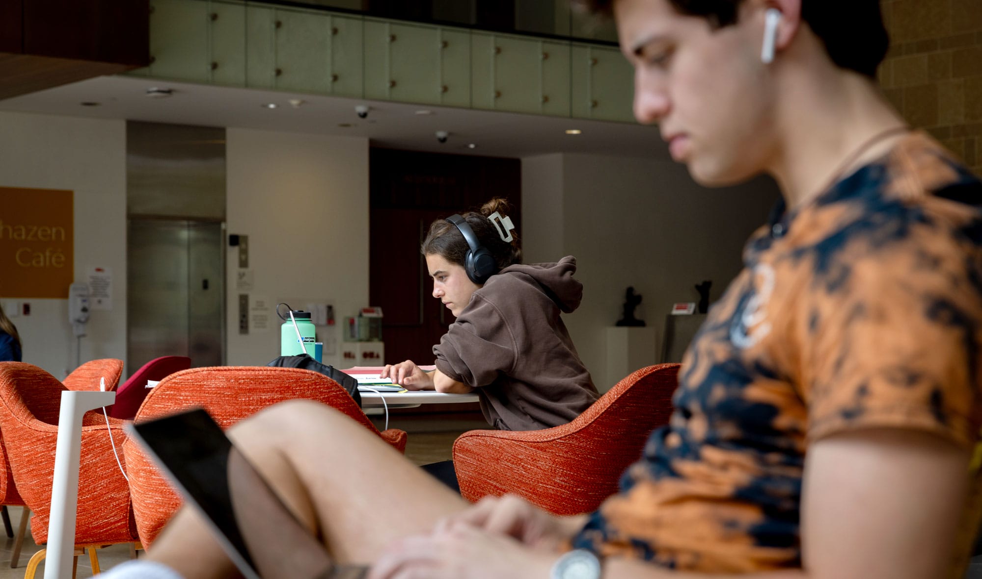 Two students wearing headphones working on their laptops.