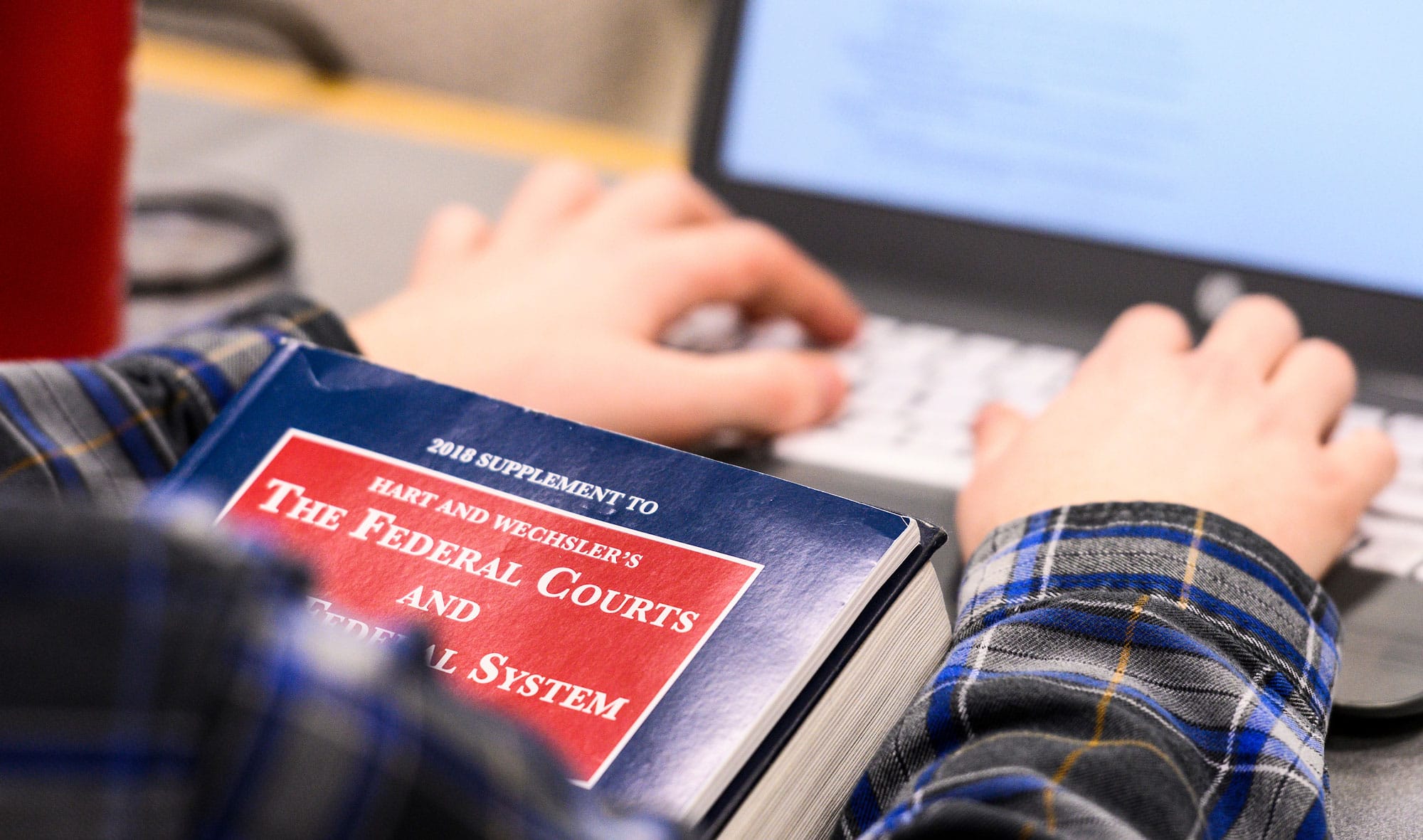 Closeup of a student typing on a laptop while consulting the book The Federal Courts and The Federal System