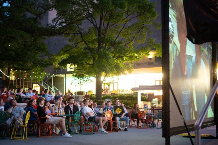 Students gathered on the UW–Madison Memorial Union Terrace sit watching a large movie screen.