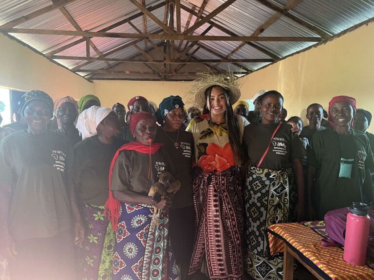 Student standing in the middle of a room surrounded by smiling people from Africa