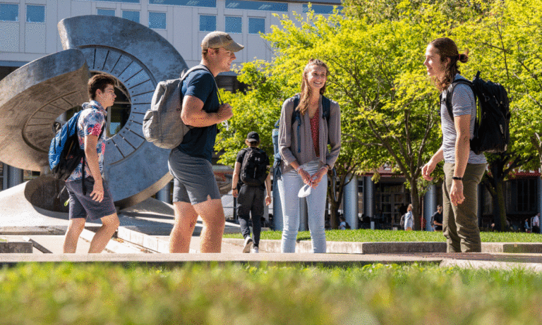 students carrying backpacks, stopping to chat and smiling in front of the UW-Madison engineering building