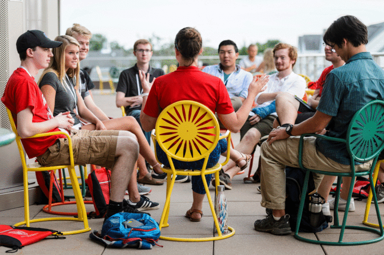 Students sitting in semi circle on terrace focused on a staff person who is talking